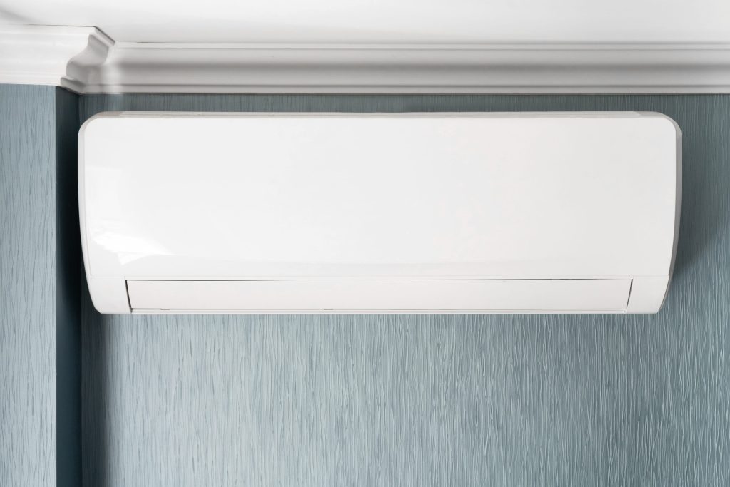A white air conditioner is installed under a white ceiling in a room with gray and blue walls.